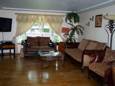 Cozy living room with leather sofas, coffee table, TV, and potted plants.