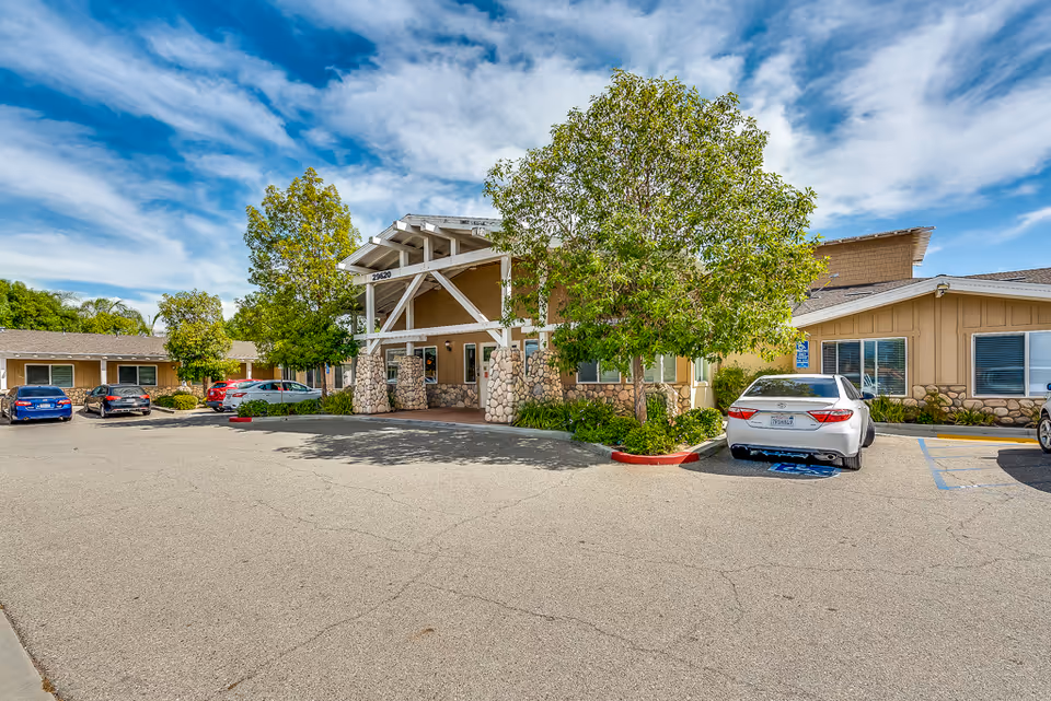 Exterior view of Sunny Rose Senior Living entrance with parked cars and landscaped entry.