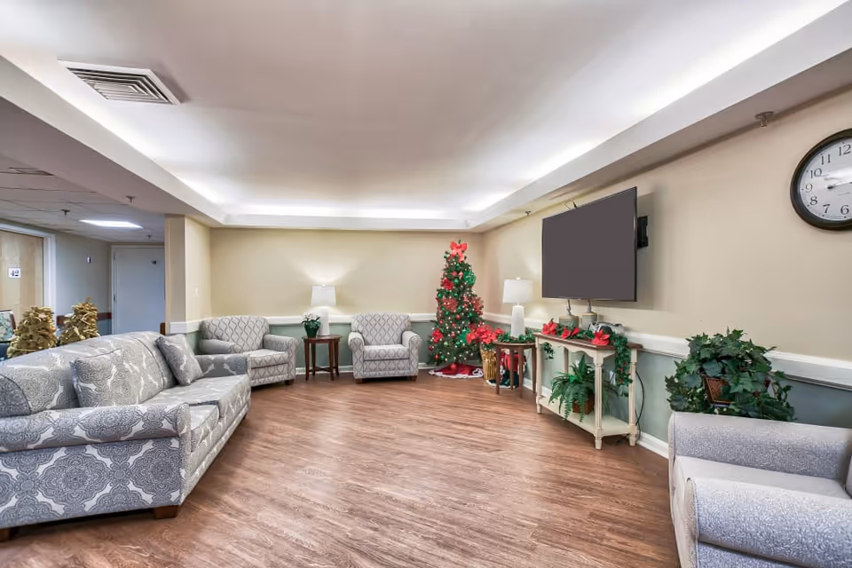 Communal living room with patterned sofas and armchairs, a wall-mounted TV, and a decorated Christmas tree.