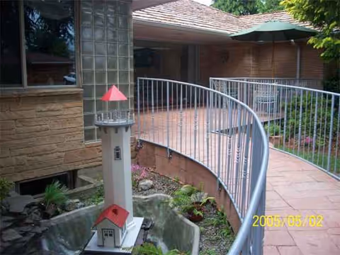 Curved metal railing borders a brick exterior walkway with a small decorative red-roofed structure.