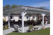 Covered outdoor pavilion with seating and tables on a lawn beside a single-story building.