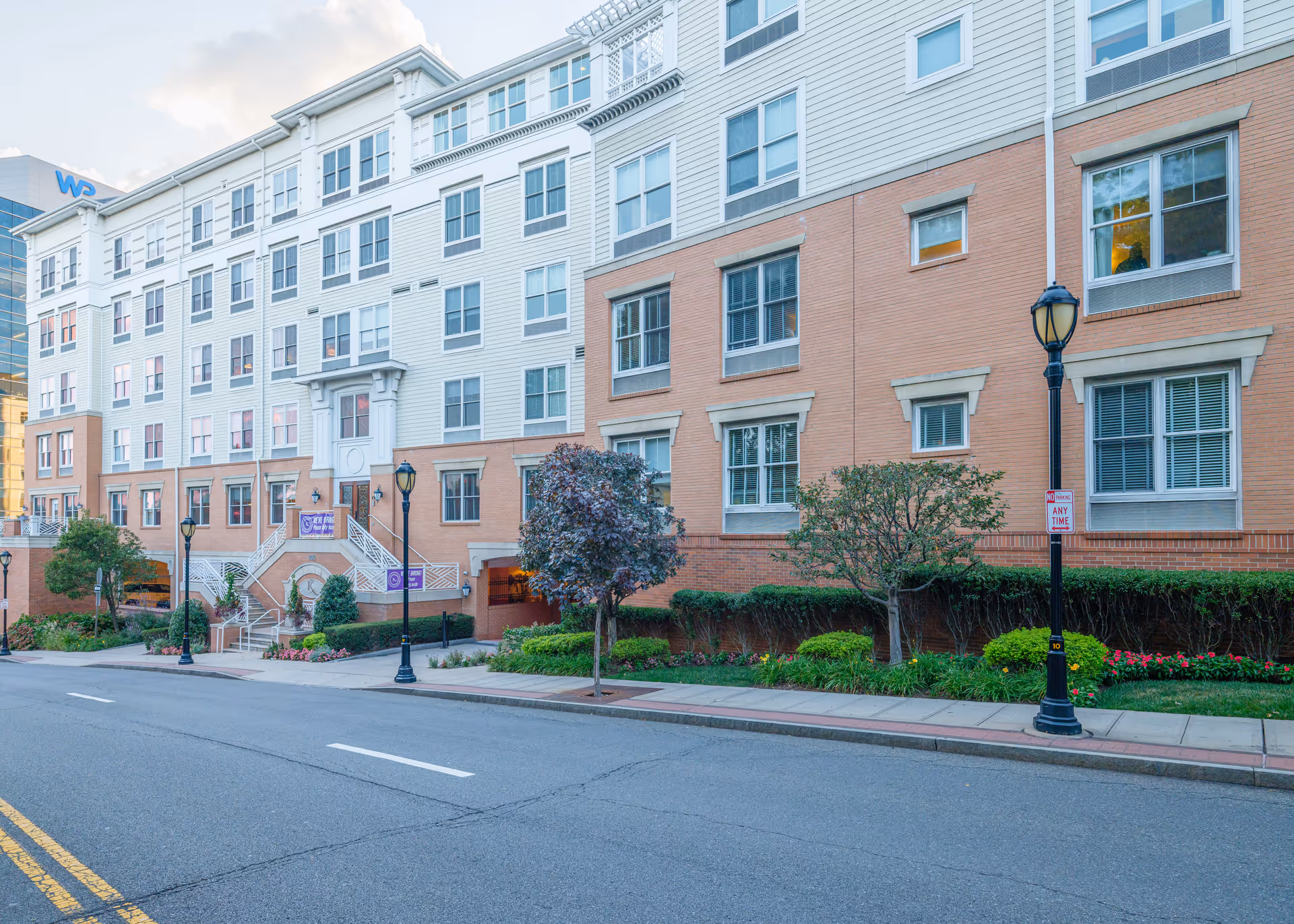 Street view of The Kensington White Plains multi-story building with a brick-and-siding façade, landscaped sidewalk, stairs to the entrance, and street lamps.