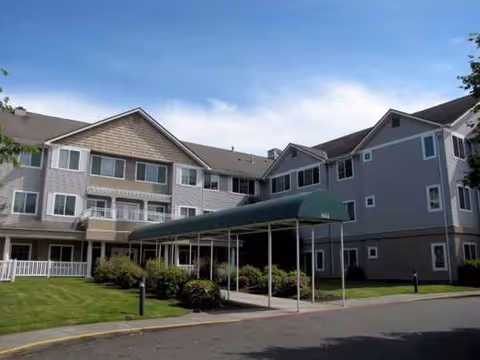 Exterior view of a senior living building with a green canopy and landscaped lawn.