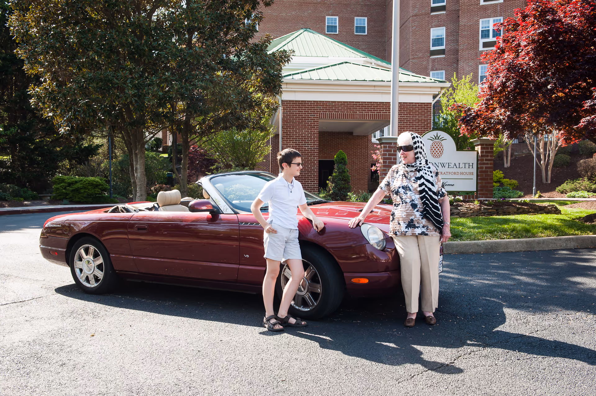 Two people stand by a red convertible outside Commonwealth Stratford House on a sunny day