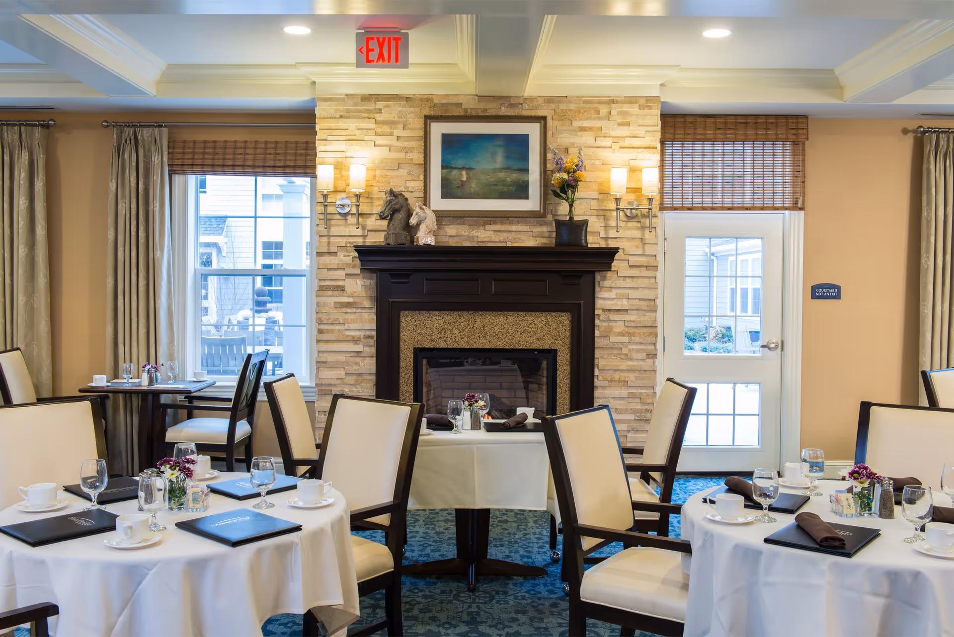 Elegant dining room with round tables set for meals, upholstered chairs, and a stone fireplace.