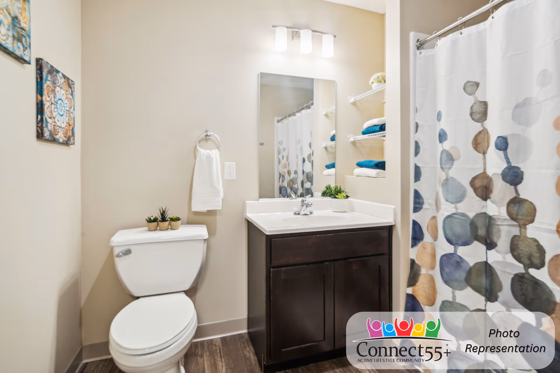 Small bathroom with a toilet, vanity with sink and mirror, shelving with towels, and a patterned shower curtain.