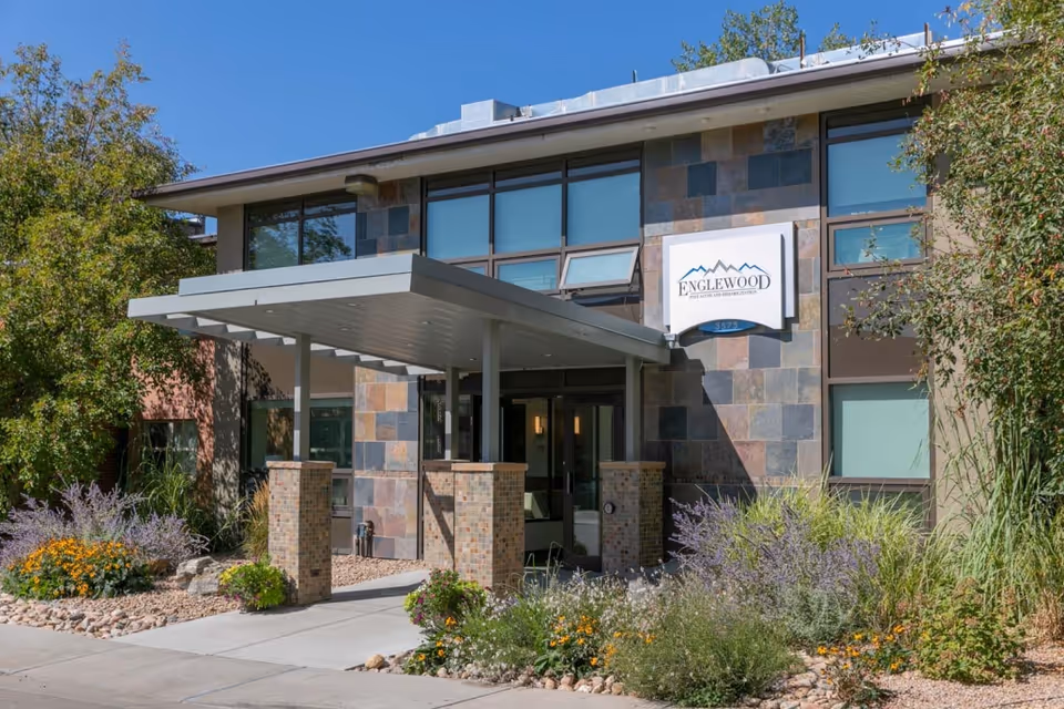 Front entrance of the Englewood Post Acute and Rehabilitation building with a covered porte-cochère, slate facade, and landscaped flower beds.
