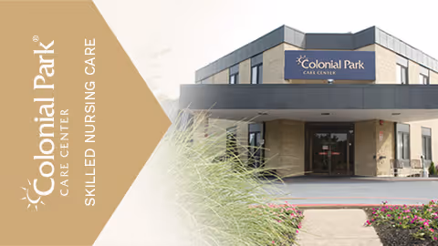 Exterior view of Colonial Park Care Center building with entrance canopy, surrounded by landscaping including grass and flowers.