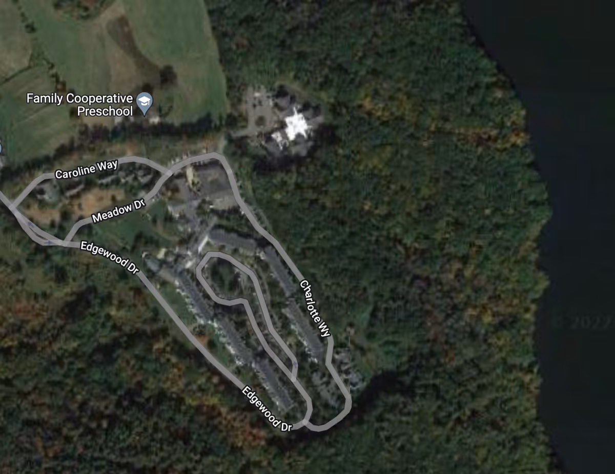 Aerial satellite view of The Woodlands Inn at Edgewood facility surrounded by dense forest and adjacent to a body of water. Roads including Caroline Way, Meadow Dr, Edgewood Dr, and Charlotte Wy are visible within the property. Nearby is the Family Cooperative Preschool.