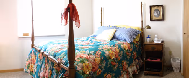 Sunlit bedroom with a wooden four-poster bed dressed in a floral bedspread and a small nightstand.