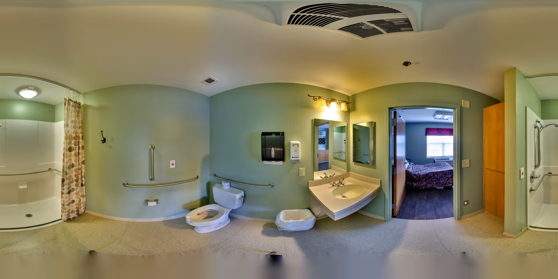 A spacious, accessible bathroom with light green walls featuring a toilet with grab bars, a sink with two mirrors and a soap dispenser, and two shower areas with curtains and grab bars. Through an open door, a bedroom with a bed and window is visible.