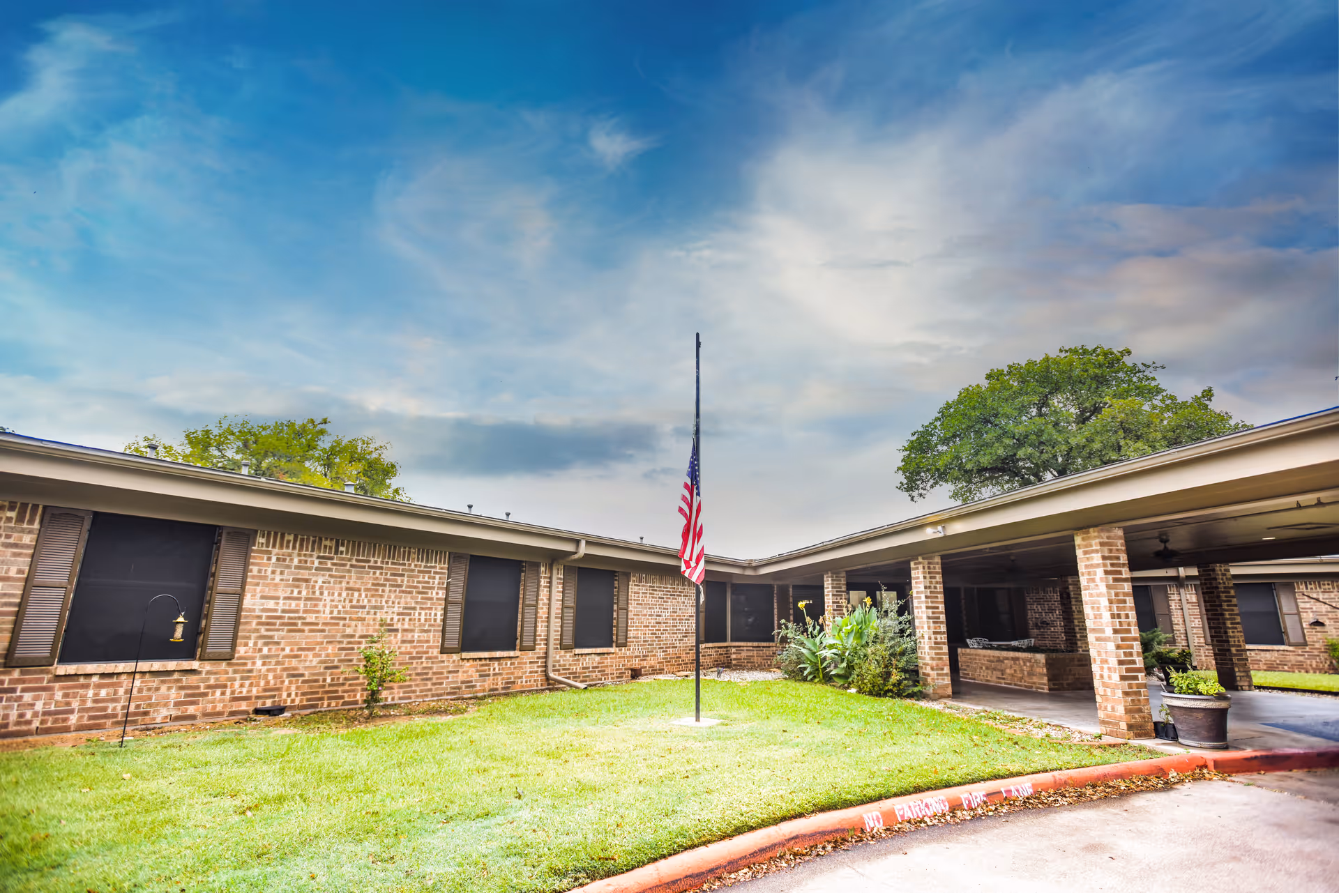 Single-story brick care facility courtyard with an American flag at half-mast and a covered entrance drive.
