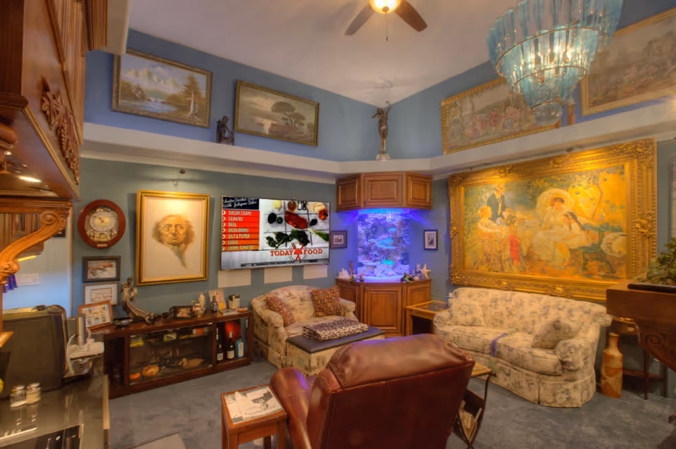 Cozy living room with sofas, an armchair, a large ornate painting, a TV, and an illuminated fish tank under decorative lighting.