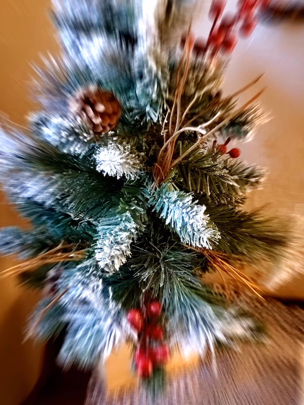 Close-up of a frosted artificial evergreen arrangement with a pine cone and red berries.