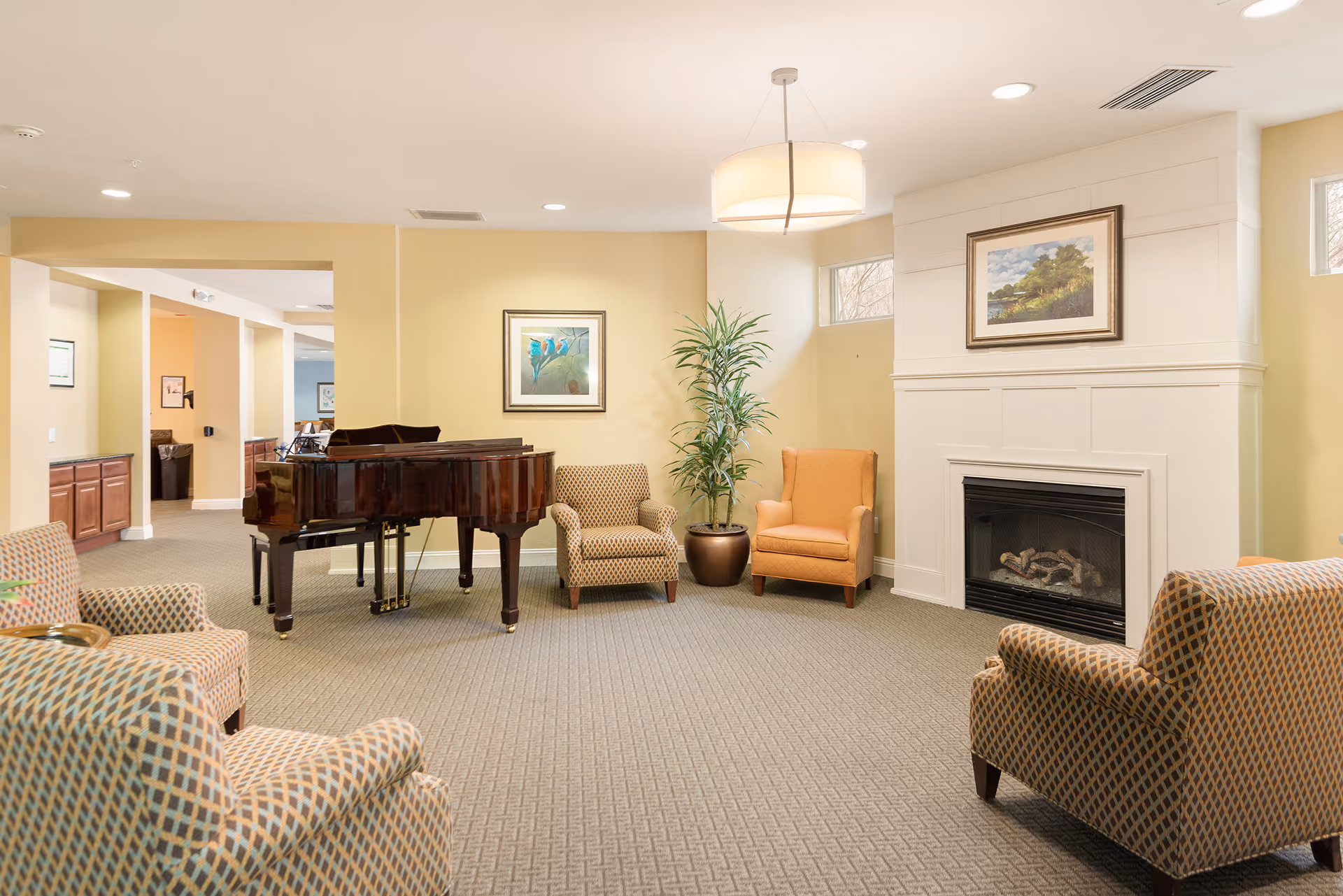 Bright common lounge with a grand piano, upholstered armchairs, a fireplace and framed artwork.