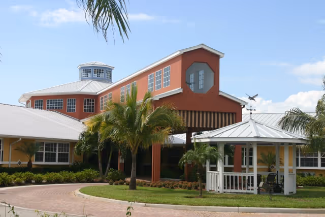Colorful senior living facility exterior with red facade, palm trees, and a white gazebo.