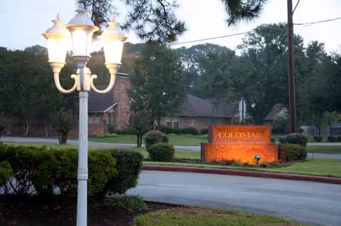 Exterior view of Colonial nursing facility sign with lamp post and landscaping.