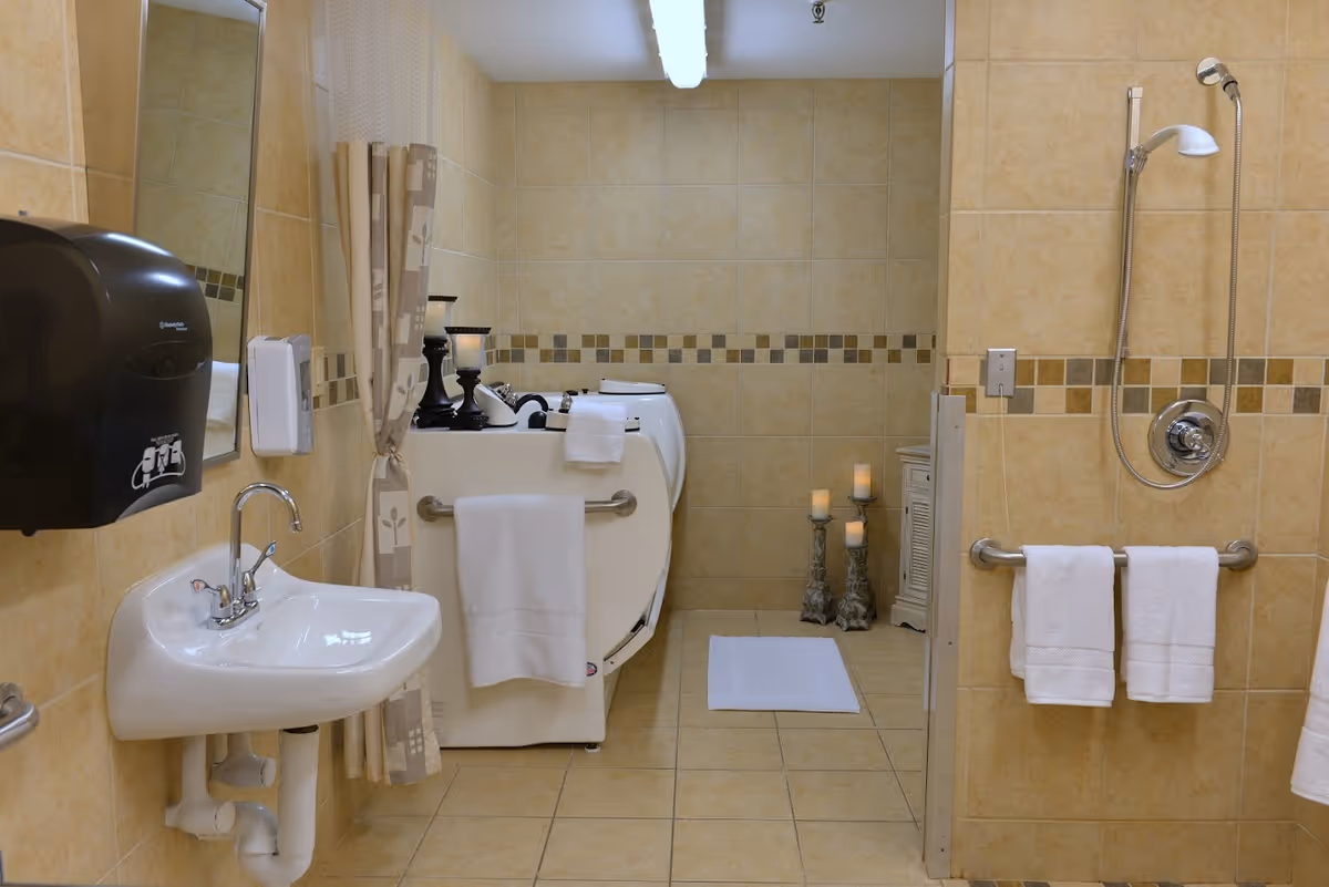 Accessible tiled bathroom with a walk-in tub, shower, sink, and towel bars holding folded towels.