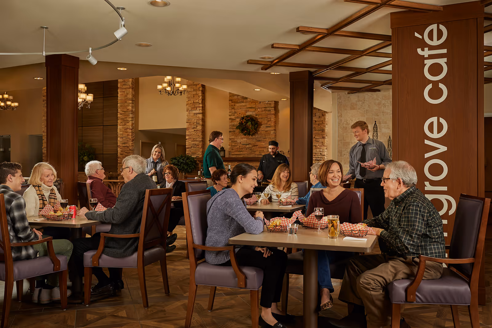 Seniors and staff sit and chat while dining in a warm, wood-accented café/dining room.