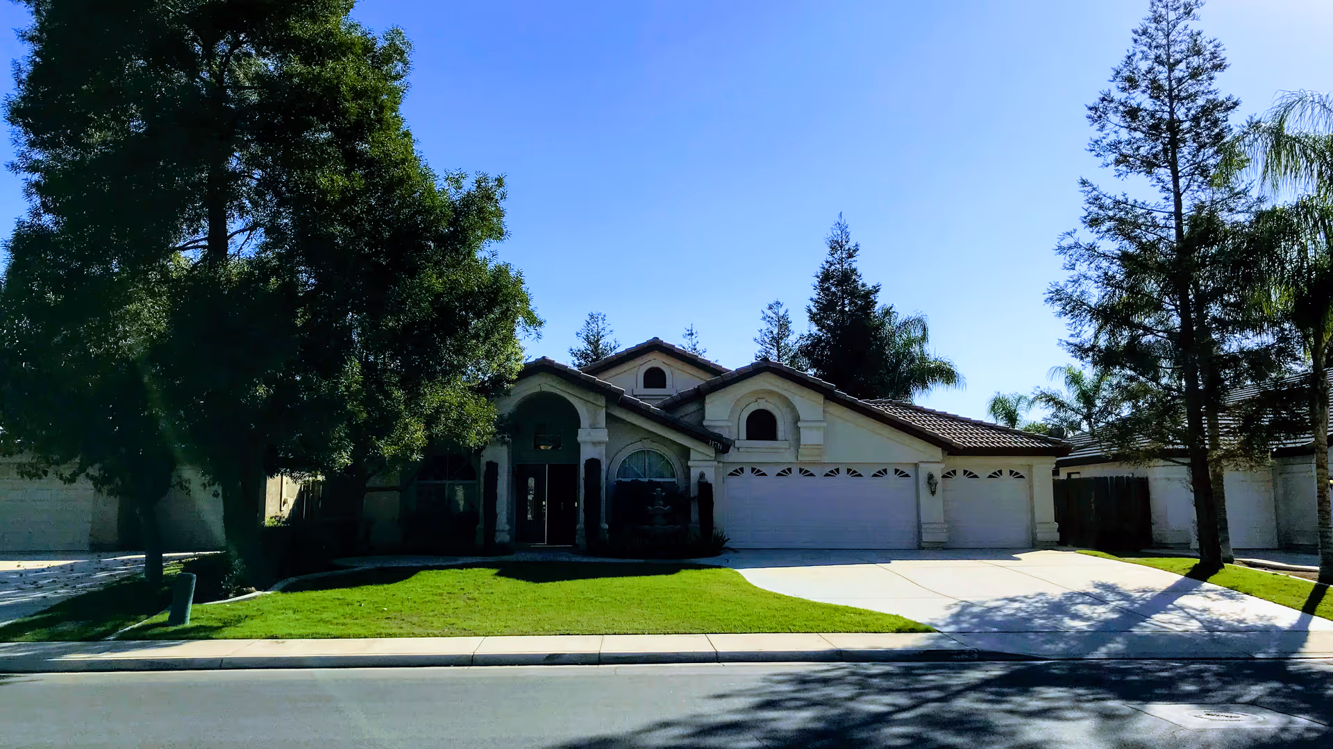 Front exterior view of a single-story residential-style building with a three-car garage, a well-maintained lawn, and several trees under a clear blue sky.