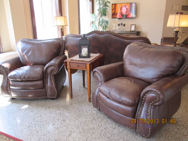 A sitting area with two brown leather armchairs, a small wooden side table with a lantern, and a wall-mounted TV in the background.