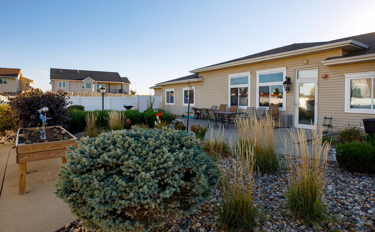 Exterior patio and landscaped courtyard with a raised planter, seating area, and a beige assisted living building in the background.