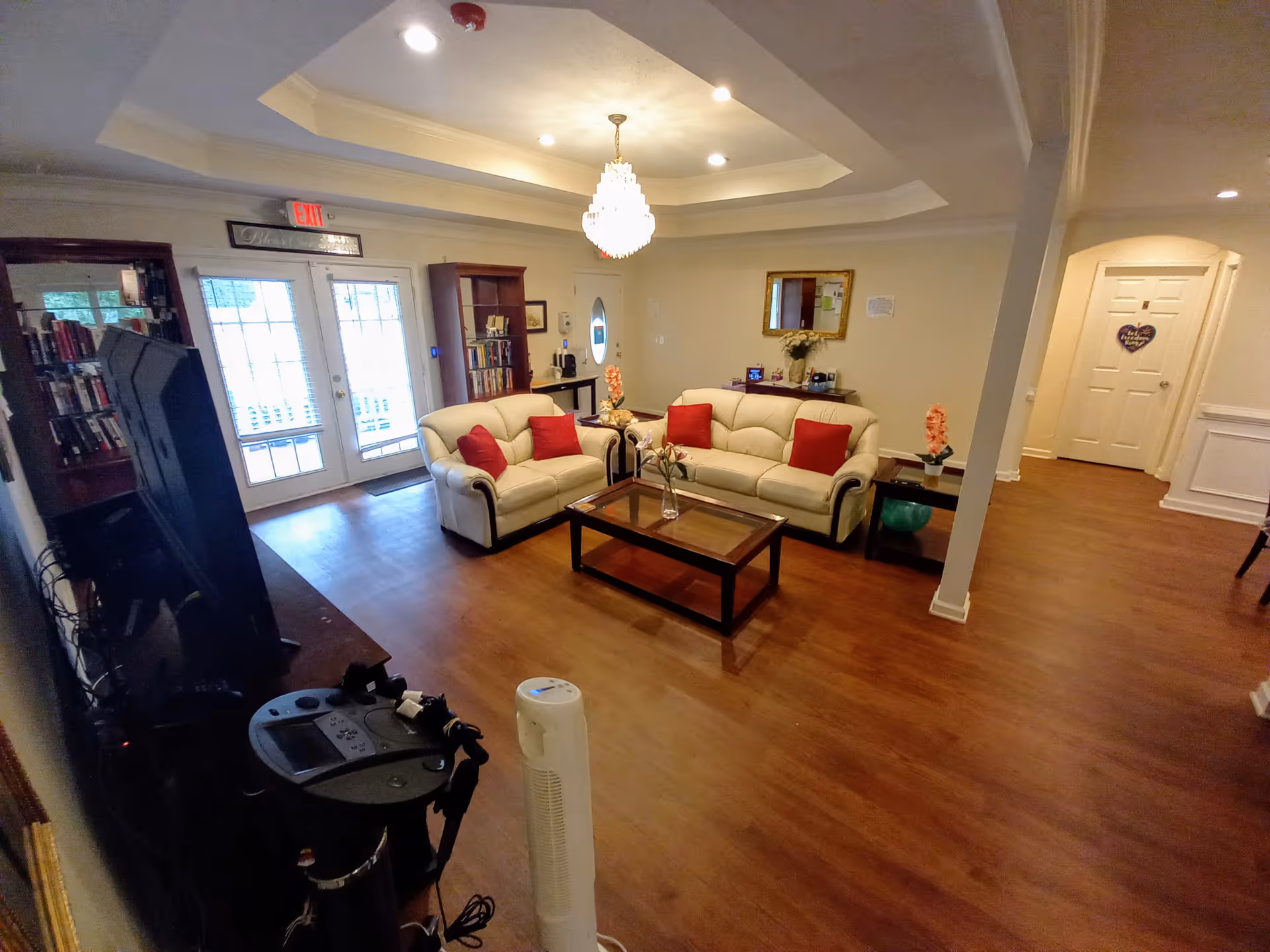 Spacious living room with two cream sofas with red pillows around a wooden coffee table, a chandelier, TV, and double glass doors.