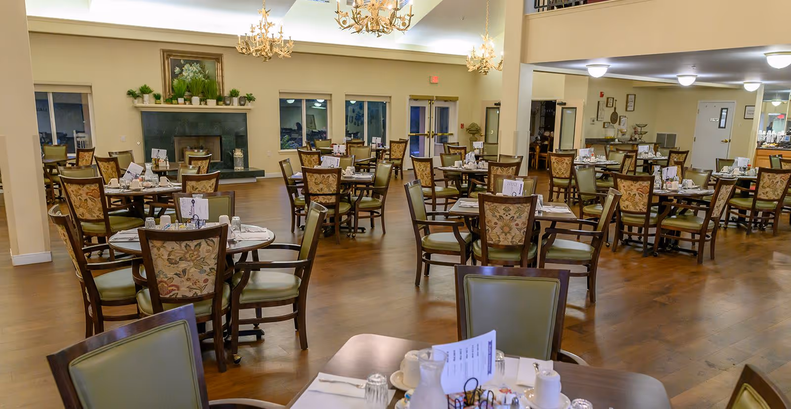 Large dining room with round tables and upholstered chairs set for service, chandeliers, and a fireplace.