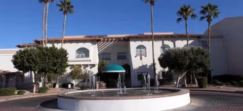Exterior view of a courtyard entrance with a circular fountain and palm trees.