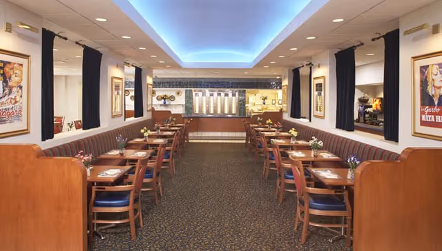 Spacious dining room with paired wooden tables and chairs lining booth seating beneath a recessed blue-lit ceiling.