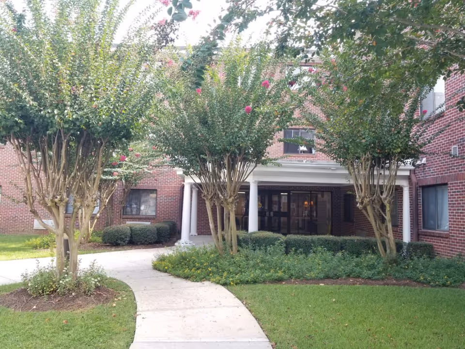 Brick senior living apartment building entrance with manicured landscaping and walkway.