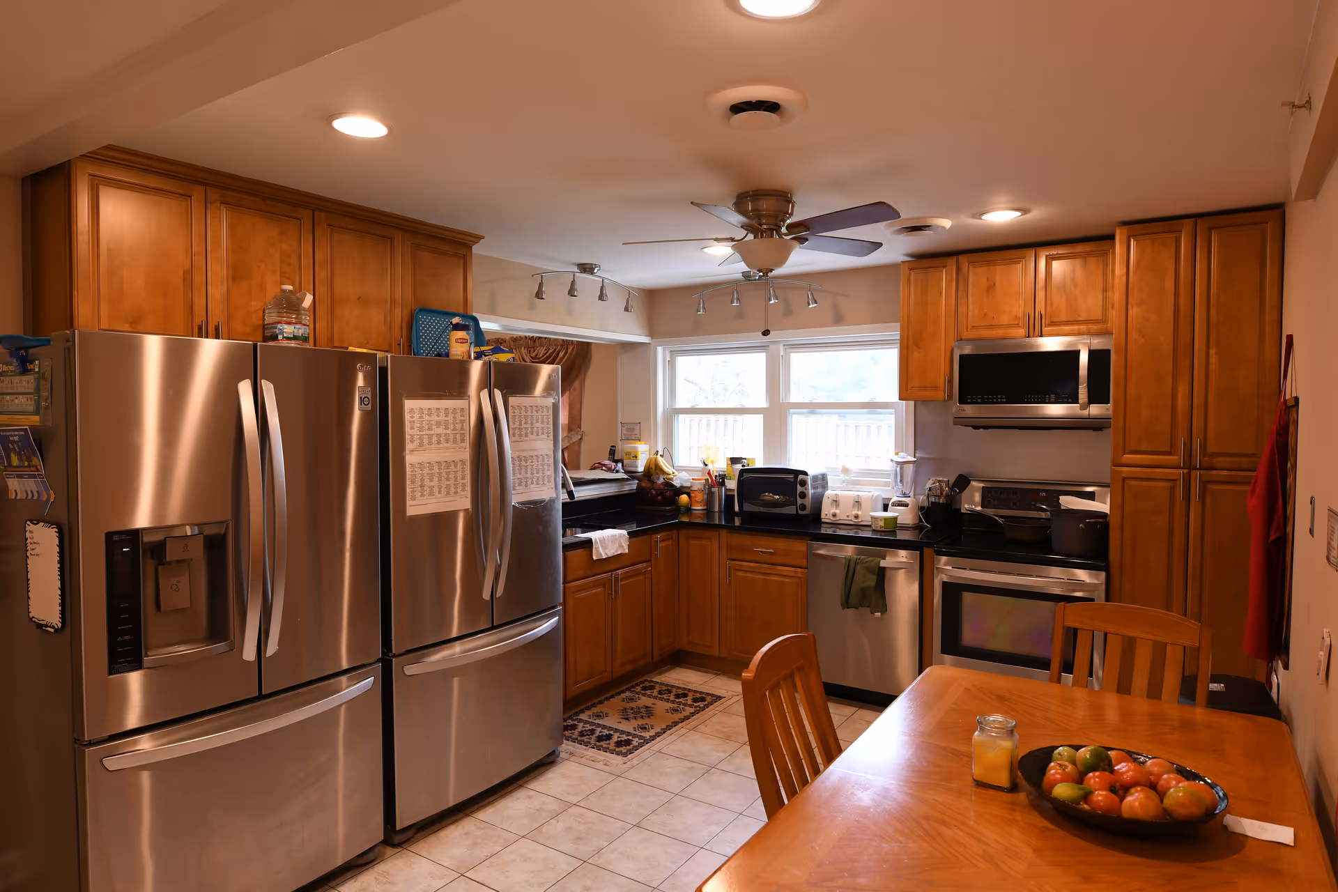 Bright kitchen with stainless steel appliances, wooden cabinets, and a dining table with a bowl of fruit.