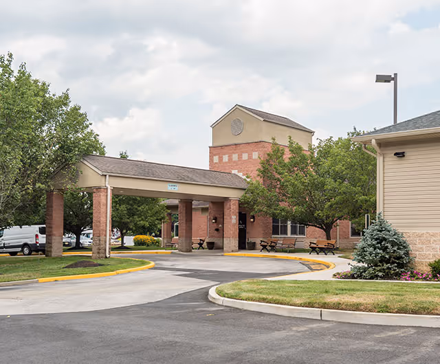 Front entrance drive-through canopy of a brick senior living facility with a circular driveway and landscaping.