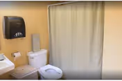 Small bathroom with a toilet, sink, paper towel dispenser, wicker hamper, and a shower with a closed curtain.