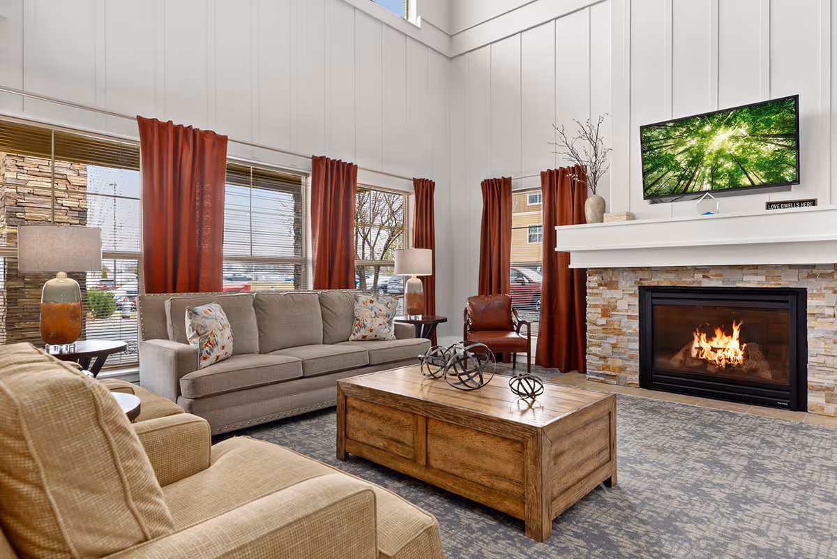 Bright communal living room with sofas, a wooden coffee table, a lit fireplace and a wall-mounted TV.