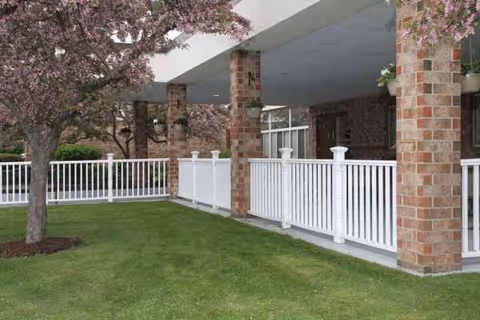 Brick facility exterior with white railing, covered walkway, and a green lawn.