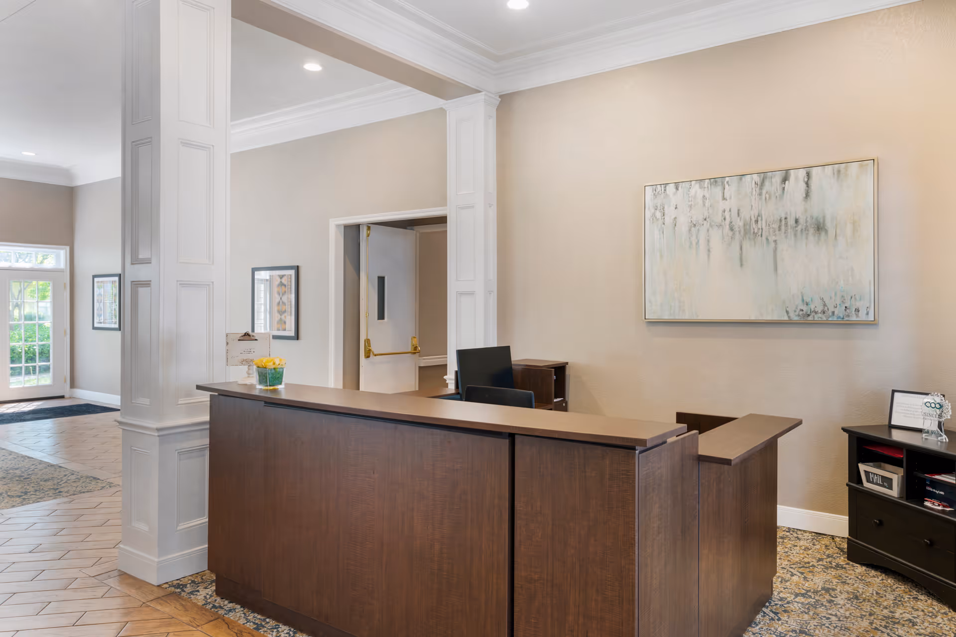 Lobby reception area with a wooden front desk, wall artwork, and entrance doors in the background.
