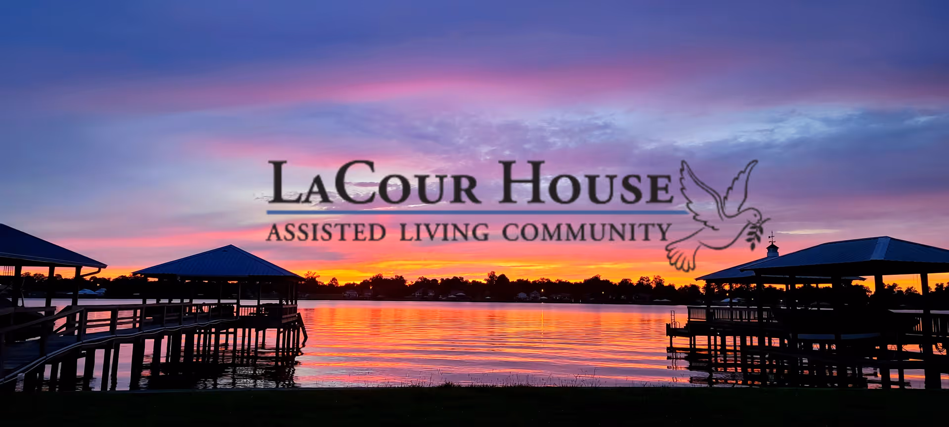 Sunset over a lake with silhouetted docks and a large overlaid LaCour House Assisted Living Community logo.
