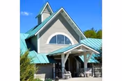 Front exterior of a senior living facility with teal roof, arched window, and covered entrance.
