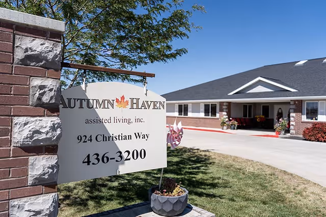 Entrance sign reading 'Autumn Haven assisted living' in front of the facility building and driveway under a clear blue sky.