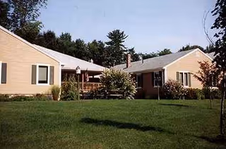 One-story building with beige siding, green lawn, and trees at a senior living facility.