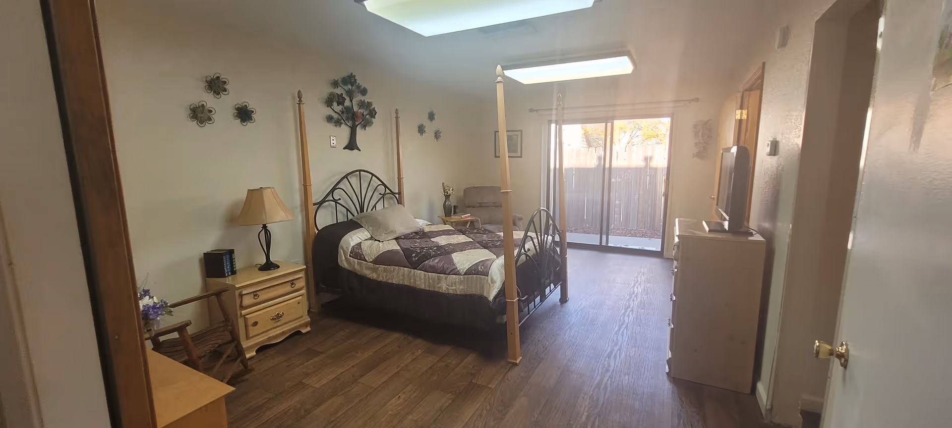 Spacious furnished bedroom with a four-post bed, nightstands and dresser, TV, wood floors and a sliding glass door to a patio.