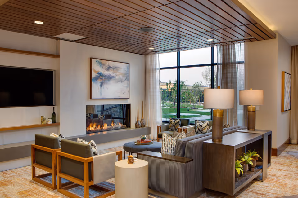 A modern lounge with sofas and armchairs around a linear fireplace and large windows overlooking a landscaped courtyard.