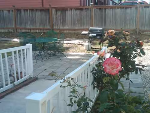 Outdoor patio with white railing, a pink rose, green table and chairs, and a grill.