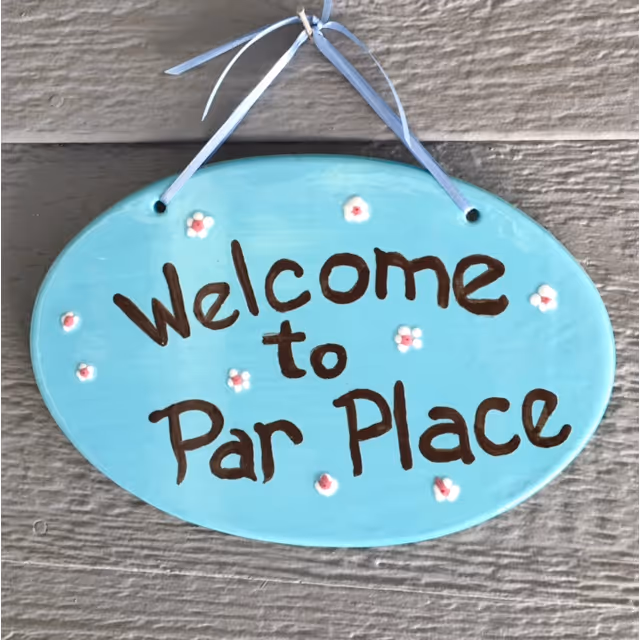 A turquoise oval welcome sign reading "Welcome to Par Place" hangs on a gray exterior wall.