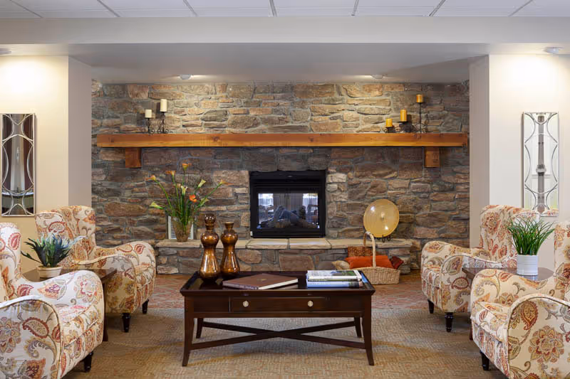 Cozy seating area with patterned armchairs arranged around a wooden coffee table facing a stone fireplace with a wooden mantel.
