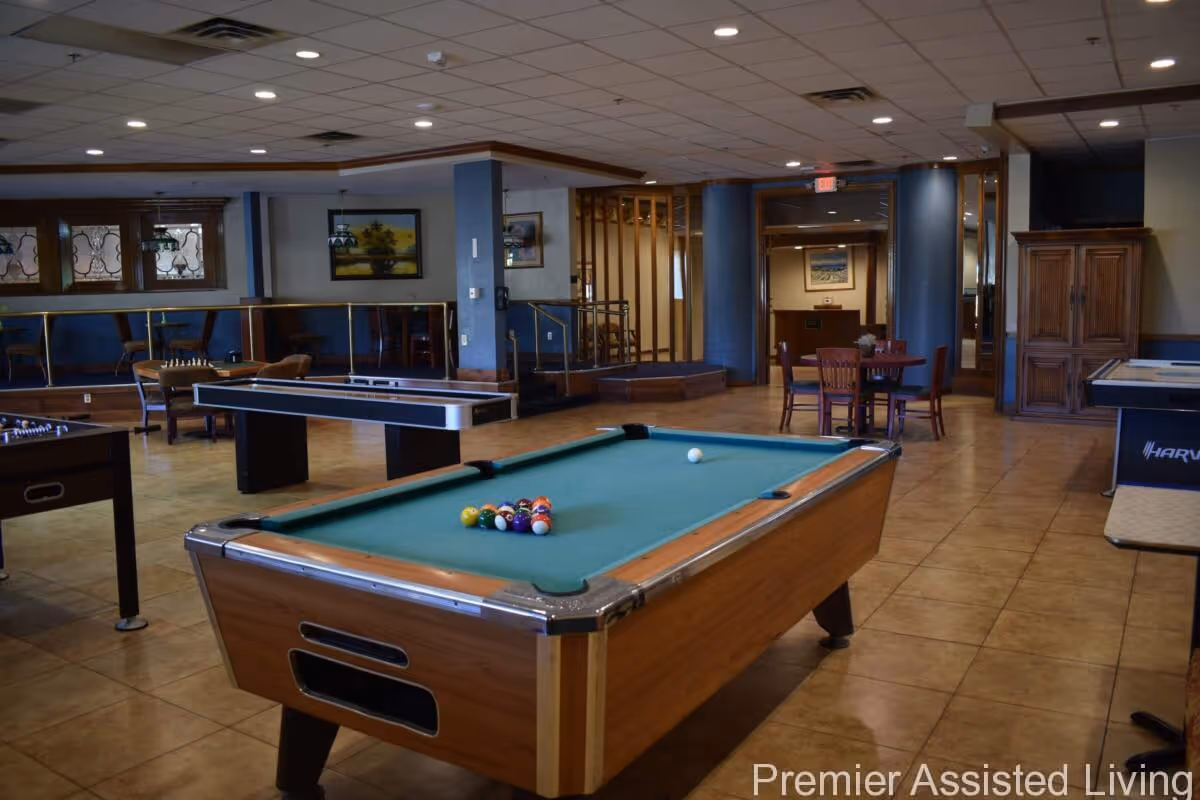 Communal game room with a pool table, shuffleboard, and seating in a senior living facility.