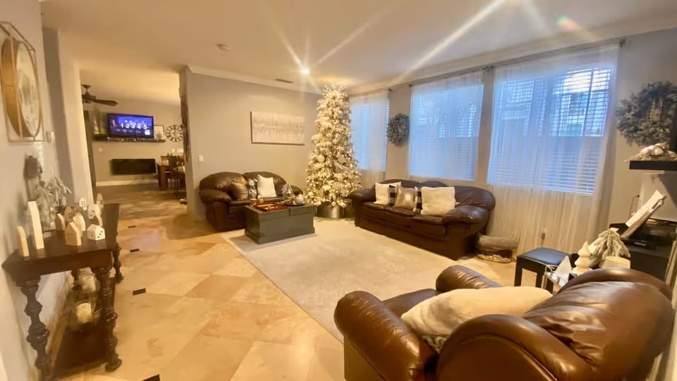 Spacious living room with leather sofas, a coffee table, and a decorated Christmas tree by large windows with blinds.