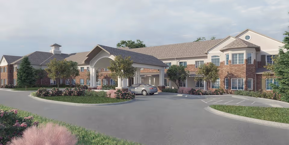 Front exterior of a two-story brick senior living facility with a covered porte-cochère, circular driveway, landscaping, and a parked car.