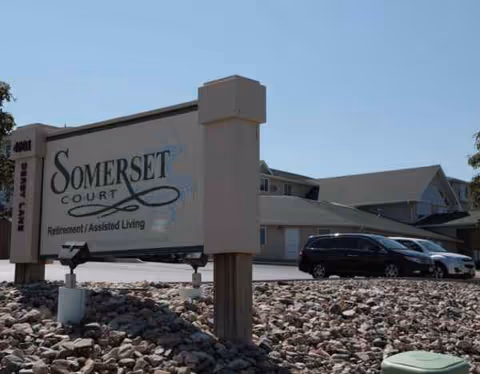 Exterior view of Somerset Court senior living facility sign with parked cars and building.